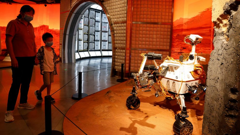 A woman and child wearing masks to curb the spread of the coronavirus look at a model depicting a rover on Mars during an exhibition in Beijing Thursday, July 23, 2020. China launched its most ambitious Mars mission yet on Thursday in a bold attempt to join the United States in successfully landing a spacecraft on the red planet. The Tianwen-1 was launched on a Long March-5 carrier rocket from a launch site on Hainan Island. (AP Photo/Ng Han Guan)